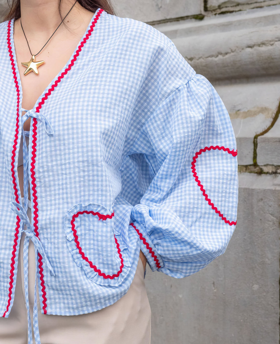 Blouse femme vichy rouge, modèle ouvert avec liens décoratifs à nouer, manches longues et finitions festonnées.