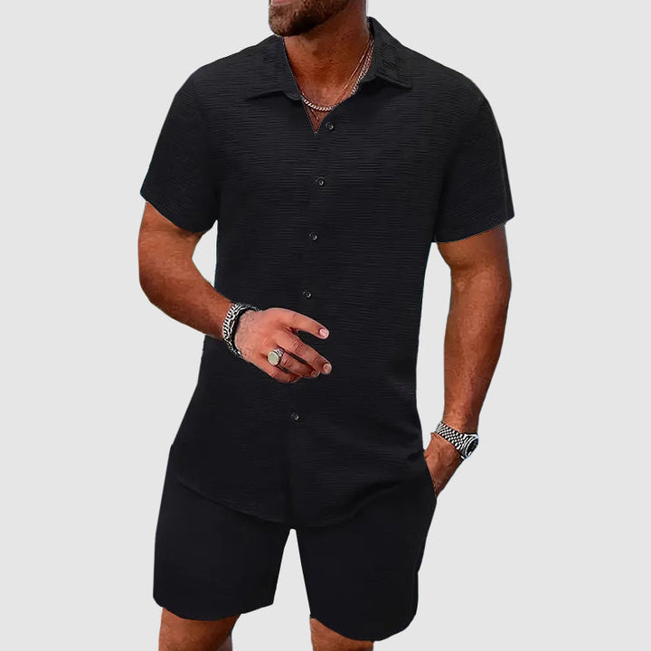 Homme portant ensemble chemise short noir décontracté. Tenue estivale confortable et moderne pour les vacances.