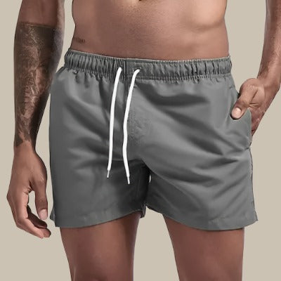 Homme souriant en short de bain, profitant de la mer, performance et look estival.